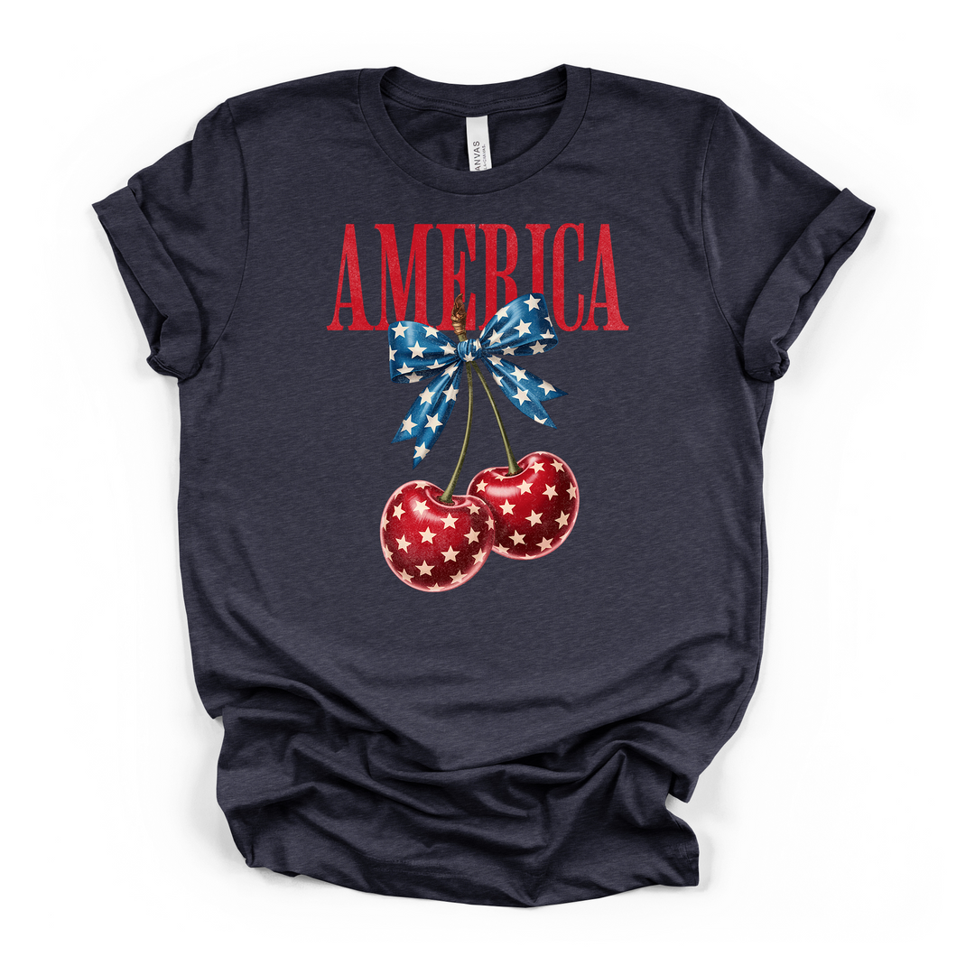 Heather navy t-shirt featuring a patriotic cherry illustration with white stars and a blue star-print bow with America text in red on the front