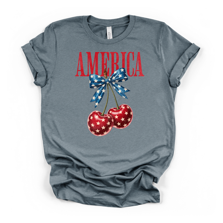 Heather slate t-shirt with a cute patriotic cherry and blue star bow graphic with America printed in distressed red lettering on the front