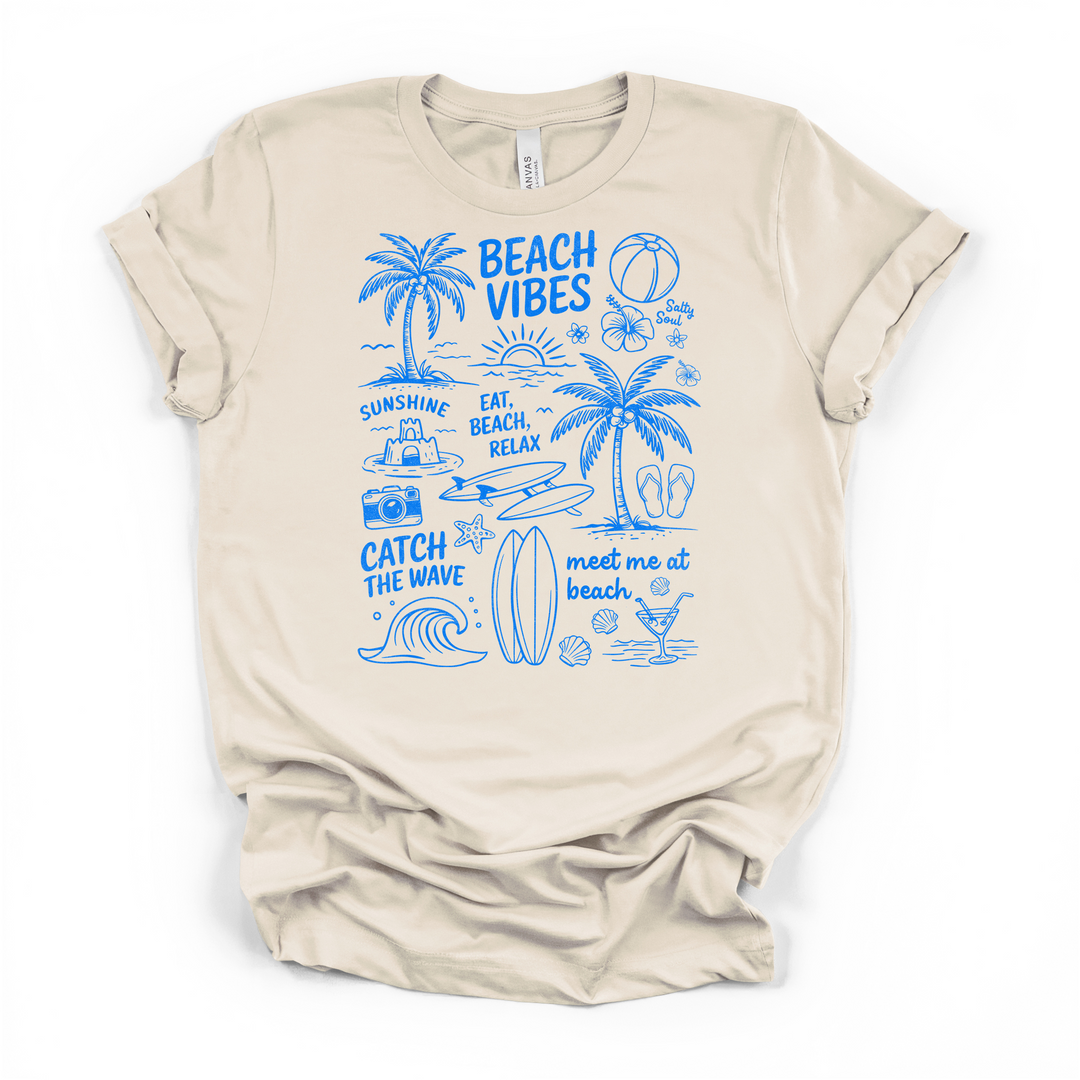 Natural cream t-shirt featuring a blue hand-drawn Beach Vibes collage with palm trees waves a surfboard sandcastle flowers and summer phrases printed on front