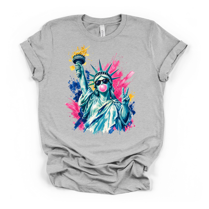 Athletic heather t-shirt with a bold pop-art watercolor Statue of Liberty wearing sunglasses blowing a pink bubble and throwing a peace sign on a colorful paint splash background