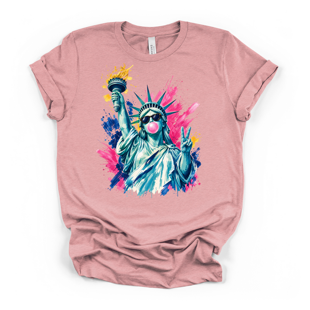 Heather pink t-shirt featuring a vibrant pop-art Lady Liberty with sunglasses blowing bubble gum and a peace sign on a pink blue and yellow paint splash background