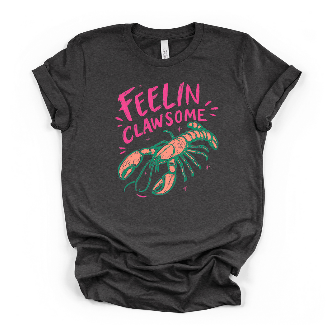 Dark grey t-shirt with a colorful coral and teal lobster graphic and pink sparkles with Feelin Clawsome printed in hot pink on the front
