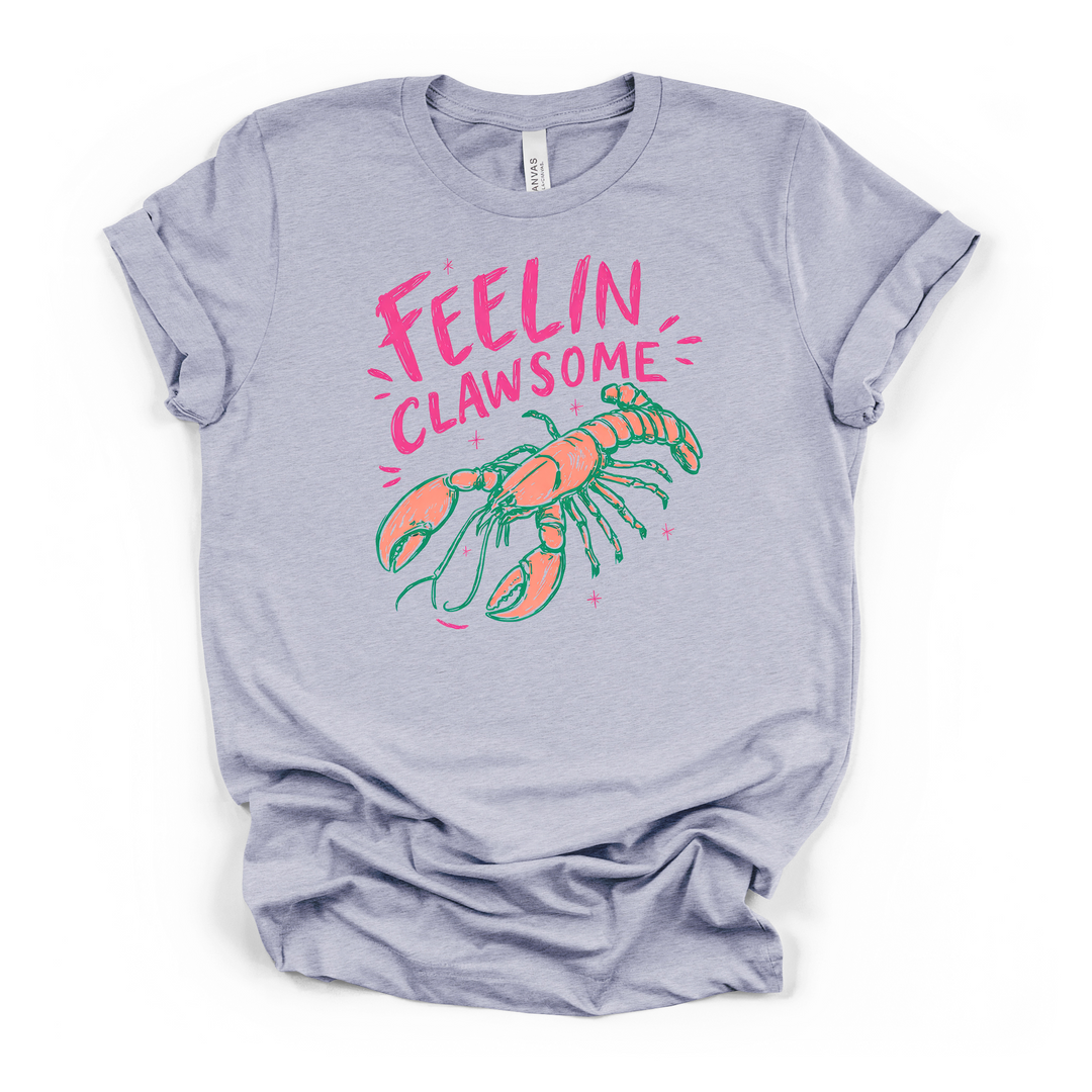 Heather blue t-shirt with a colorful illustrated lobster in coral and teal with sparkles and Feelin Clawsome printed in hot pink on the front