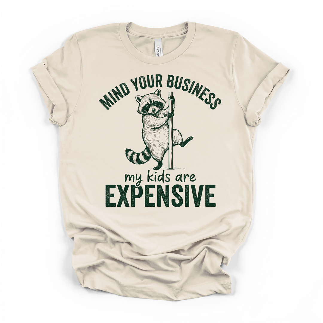 Natural cream t-shirt with a raccoon holding a pole graphic and Mind Your Business My Kids Are Expensive printed in dark green text