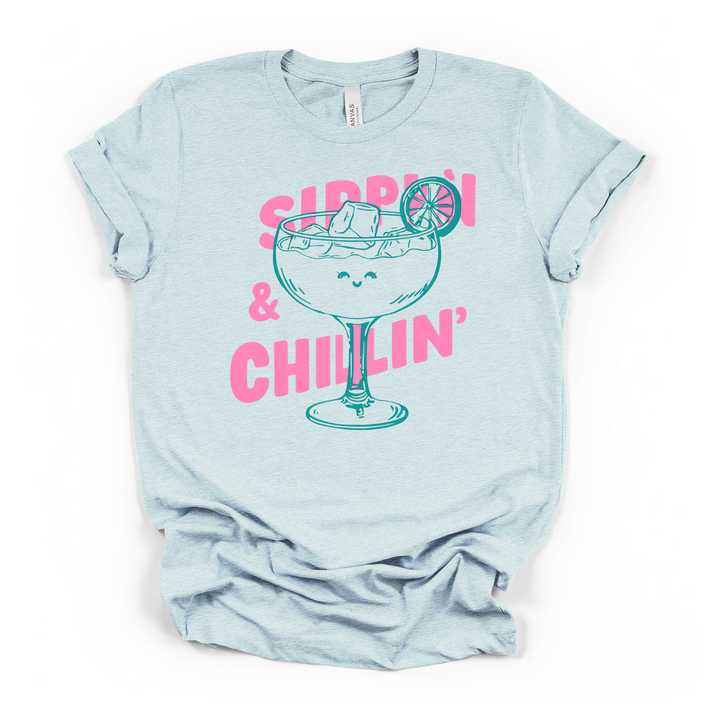 Sippin and Chillin cocktail graphic t-shirt in heather ice blue with smiling margarita glass and bold pink lettering
