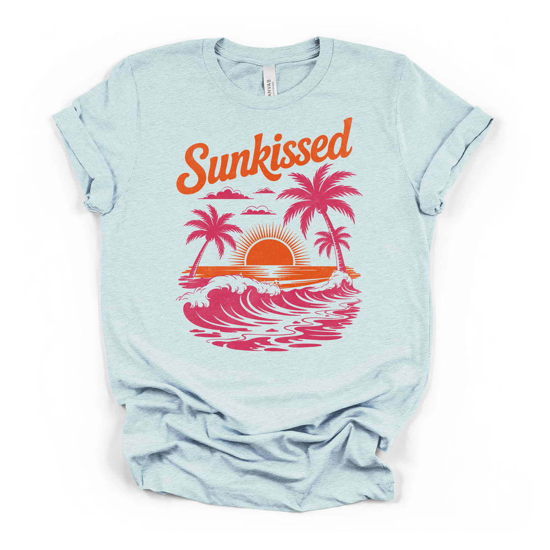 Heather ice blue t-shirt with a bold retro Sunkissed graphic with pink palm tree silhouettes crashing waves and an orange sunset printed on front
