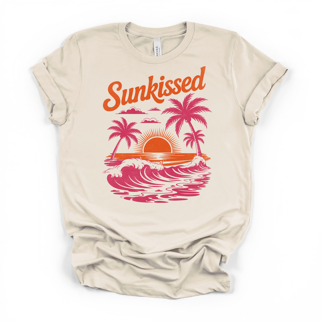 Natural cream t-shirt with a retro Sunkissed graphic featuring pink palm tree silhouettes ocean waves and an orange sunset printed on the front