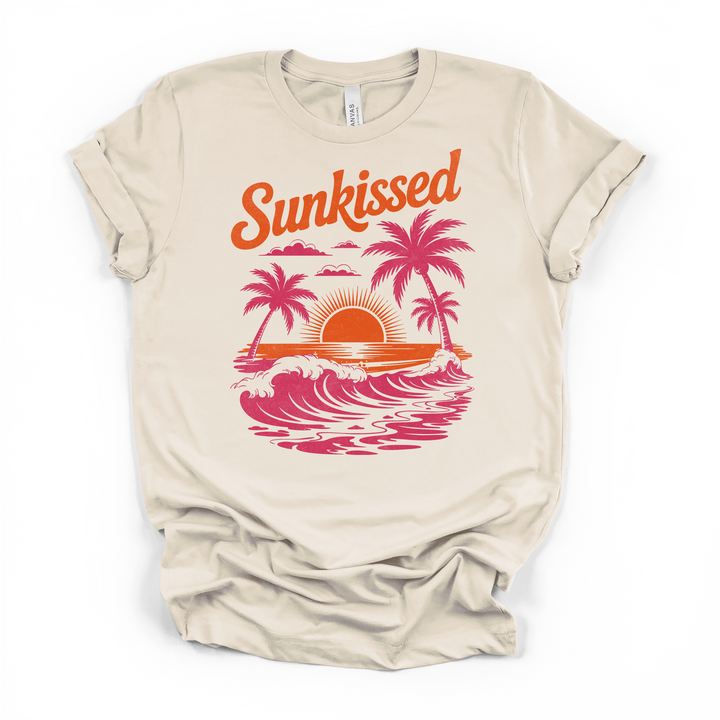 Natural cream t-shirt with a retro Sunkissed graphic featuring pink palm tree silhouettes ocean waves and an orange sunset printed on the front