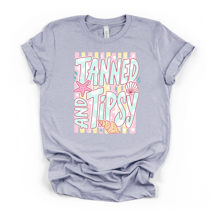 Heather blue t-shirt featuring a pastel Tanned and Tipsy beach graphic with bold retro text seashells and a starfish printed on the front