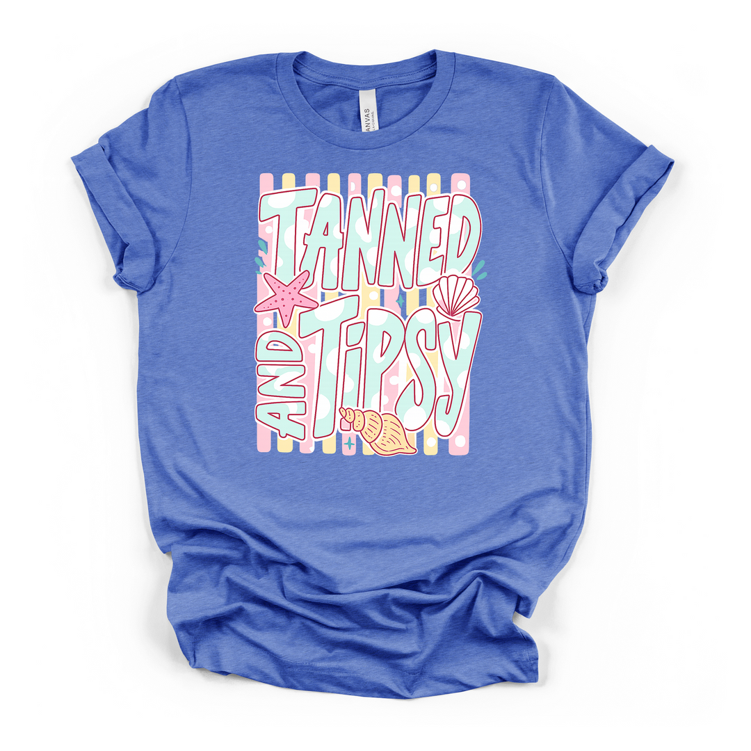 Heather columbia blue t-shirt with a fun pastel Tanned and Tipsy retro lettering graphic with shells and starfish on a striped background