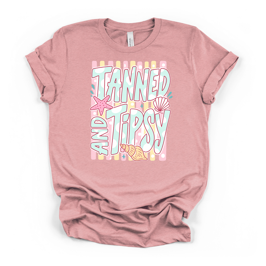 Heather pink t-shirt with a colorful pastel Tanned and Tipsy beach graphic with seashells and a starfish on a striped dotted background