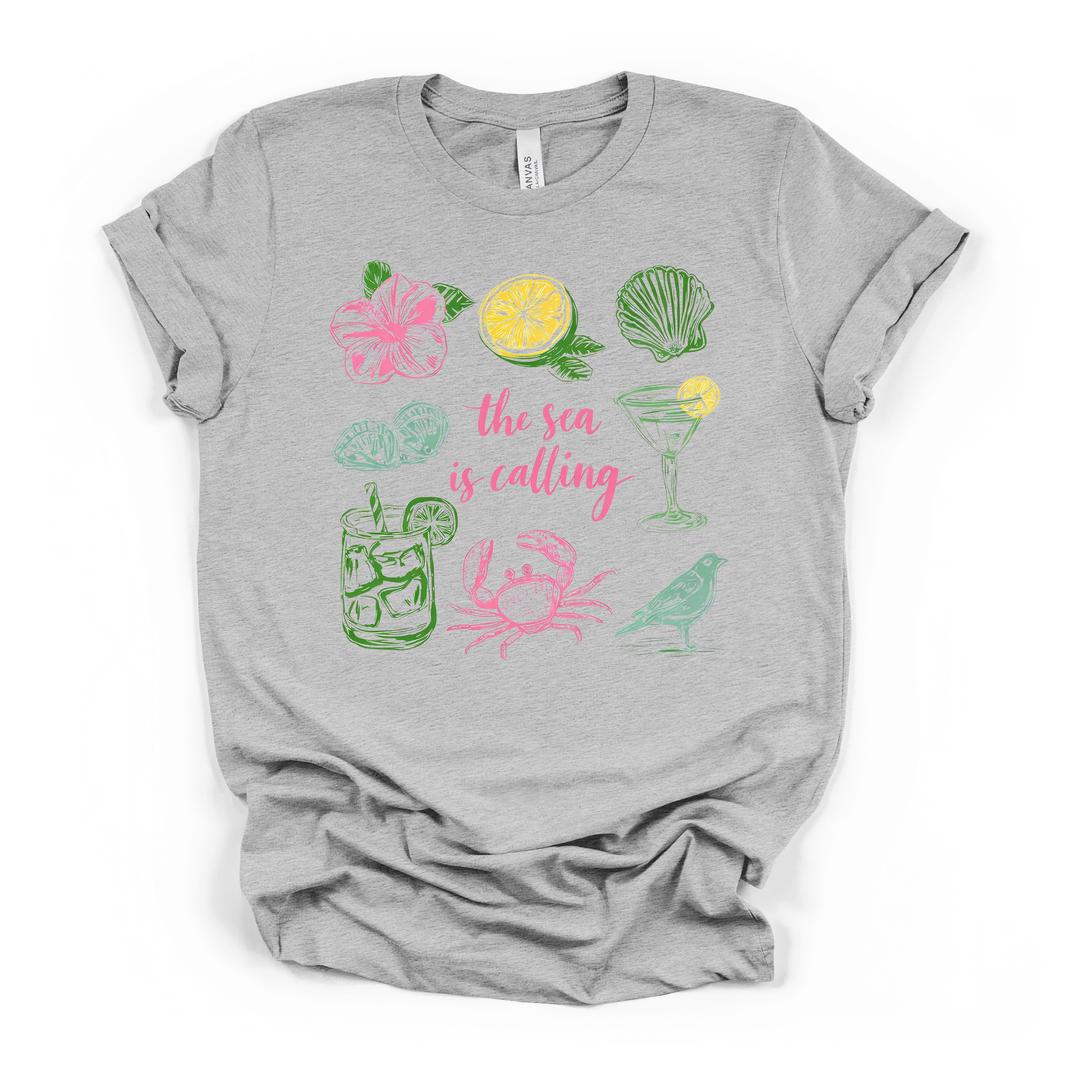 The Sea is Calling beach graphic t-shirt in athletic heather with colorful coastal icons including crab, seashell, hibiscus, and cocktails
