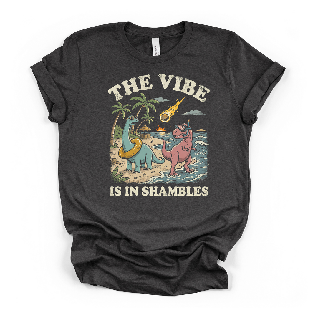 Dark grey t-shirt with a funny retro illustration of two beach dinosaurs and a falling meteor with The Vibe Is In Shambles printed on front