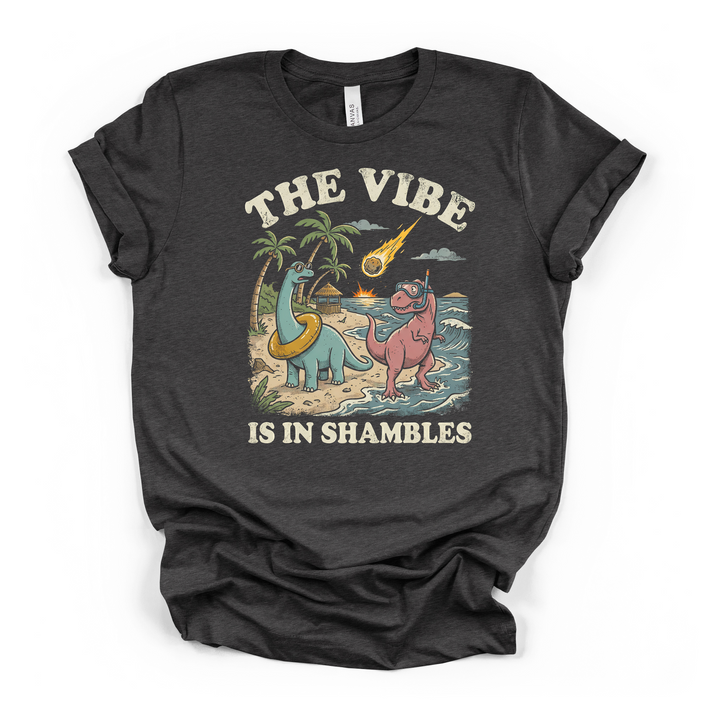 Dark grey t-shirt with a funny retro illustration of two beach dinosaurs and a falling meteor with The Vibe Is In Shambles printed on front