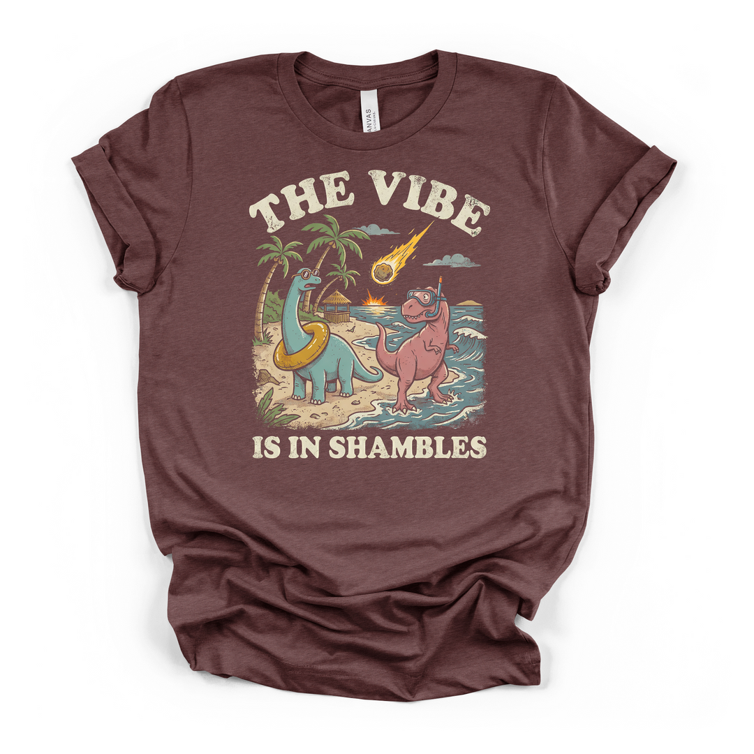 Heather maroon t-shirt featuring a vintage-style dinosaur beach scene with a falling meteor and The Vibe Is In Shambles printed on the front