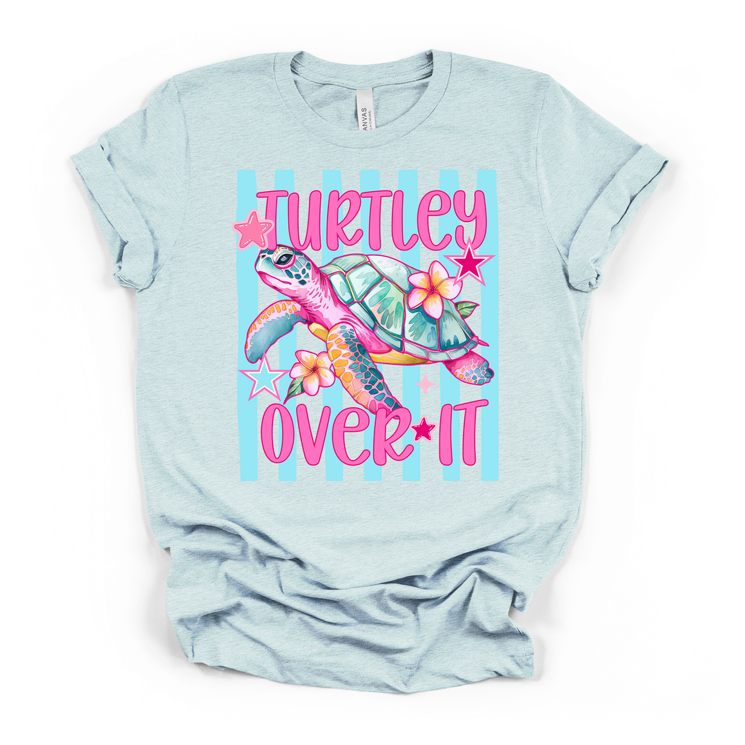 Heather ice blue t-shirt with a fun pink and teal sea turtle graphic with plumeria flowers and stars on a striped background and Turtley Over It text