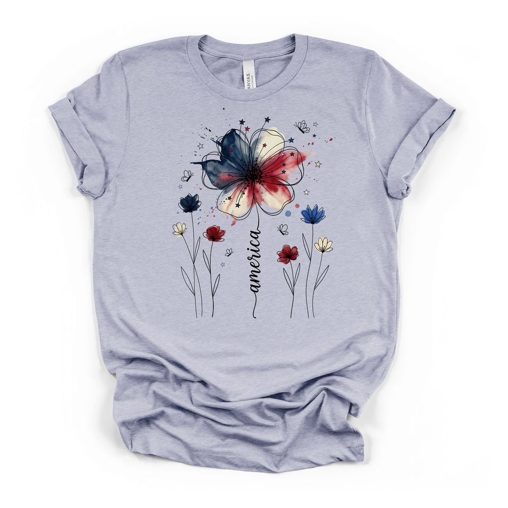 Heather blue t-shirt featuring a patriotic watercolor flower in red white and blue with delicate wildflowers stars and America written in script on the front