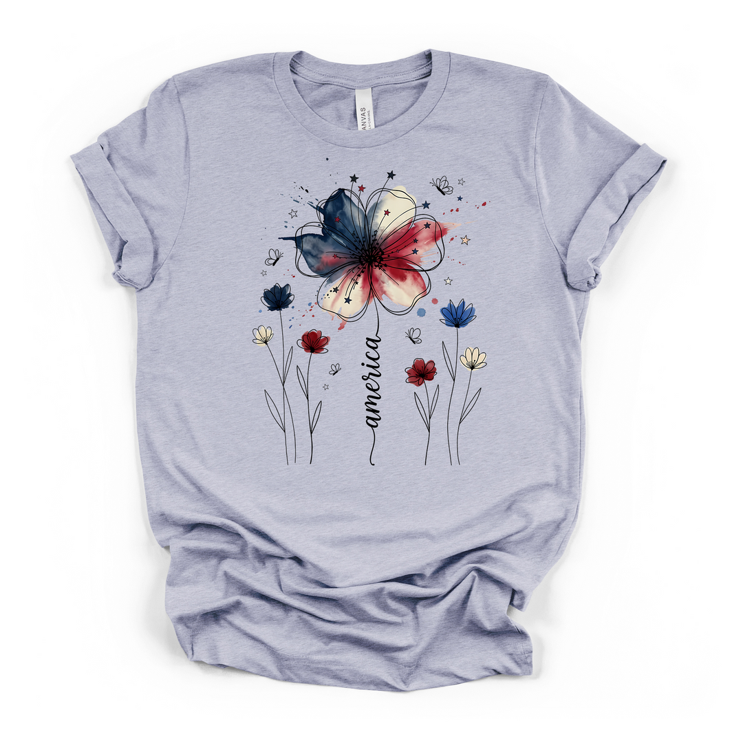 Heather blue t-shirt featuring a patriotic watercolor flower in red white and blue with delicate wildflowers stars and America written in script on the front