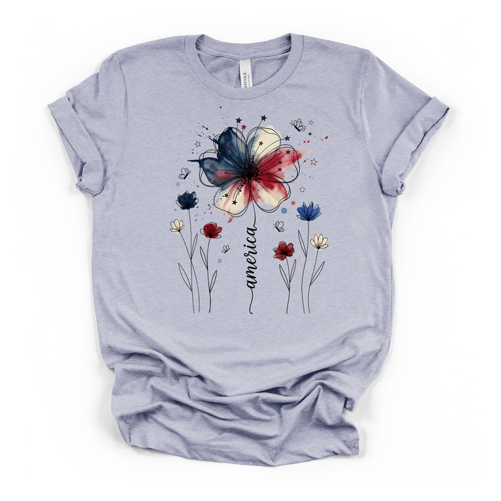 Heather blue t-shirt featuring a patriotic watercolor flower in red white and blue with delicate wildflowers stars and America written in script on the front
