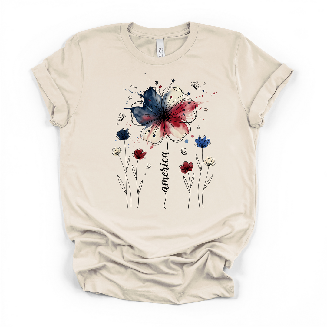 Natural cream t-shirt with a patriotic watercolor floral graphic featuring a red white and blue wildflower stars and America written in elegant script along the stem