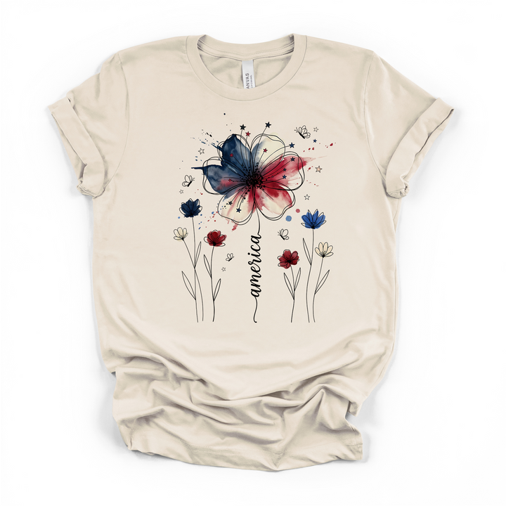 Natural cream t-shirt with a patriotic watercolor floral graphic featuring a red white and blue wildflower stars and America written in elegant script along the stem
